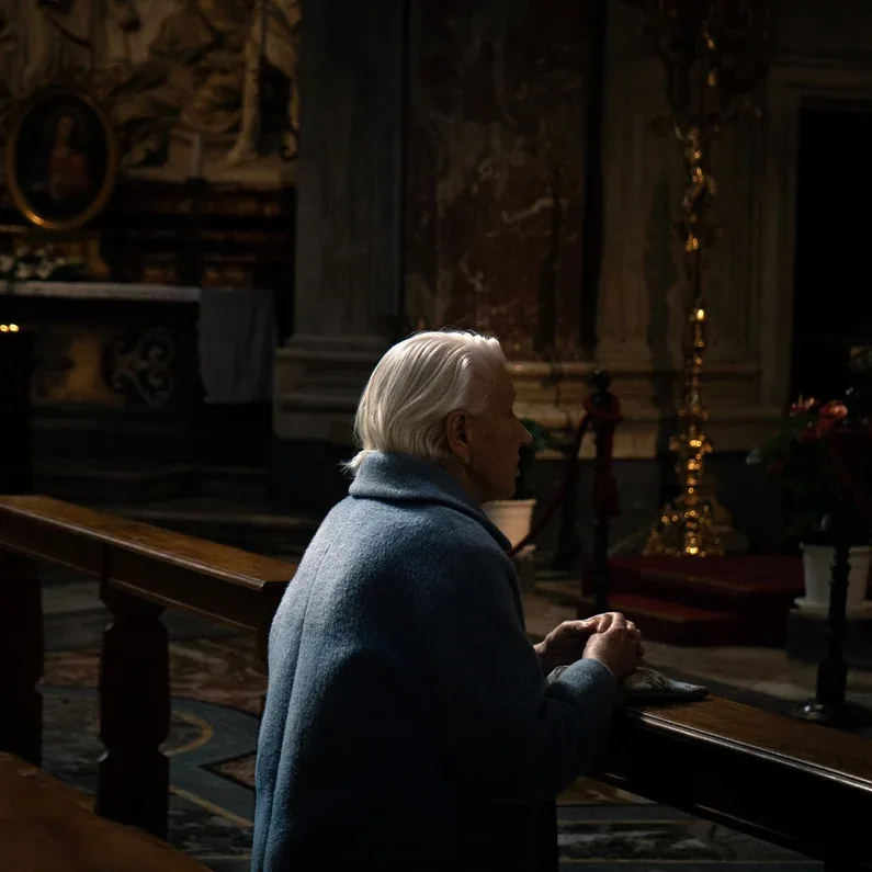 Una donna seduta su un banco in chiesa, illuminata di lato